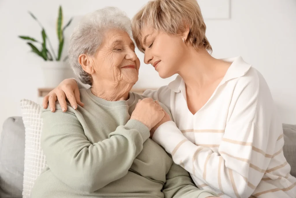 Ältere und jüngere Frau lächeln sich zärtlich an und umarmen sich. Symbol für Liebe, Fürsorge und Familienbande.
